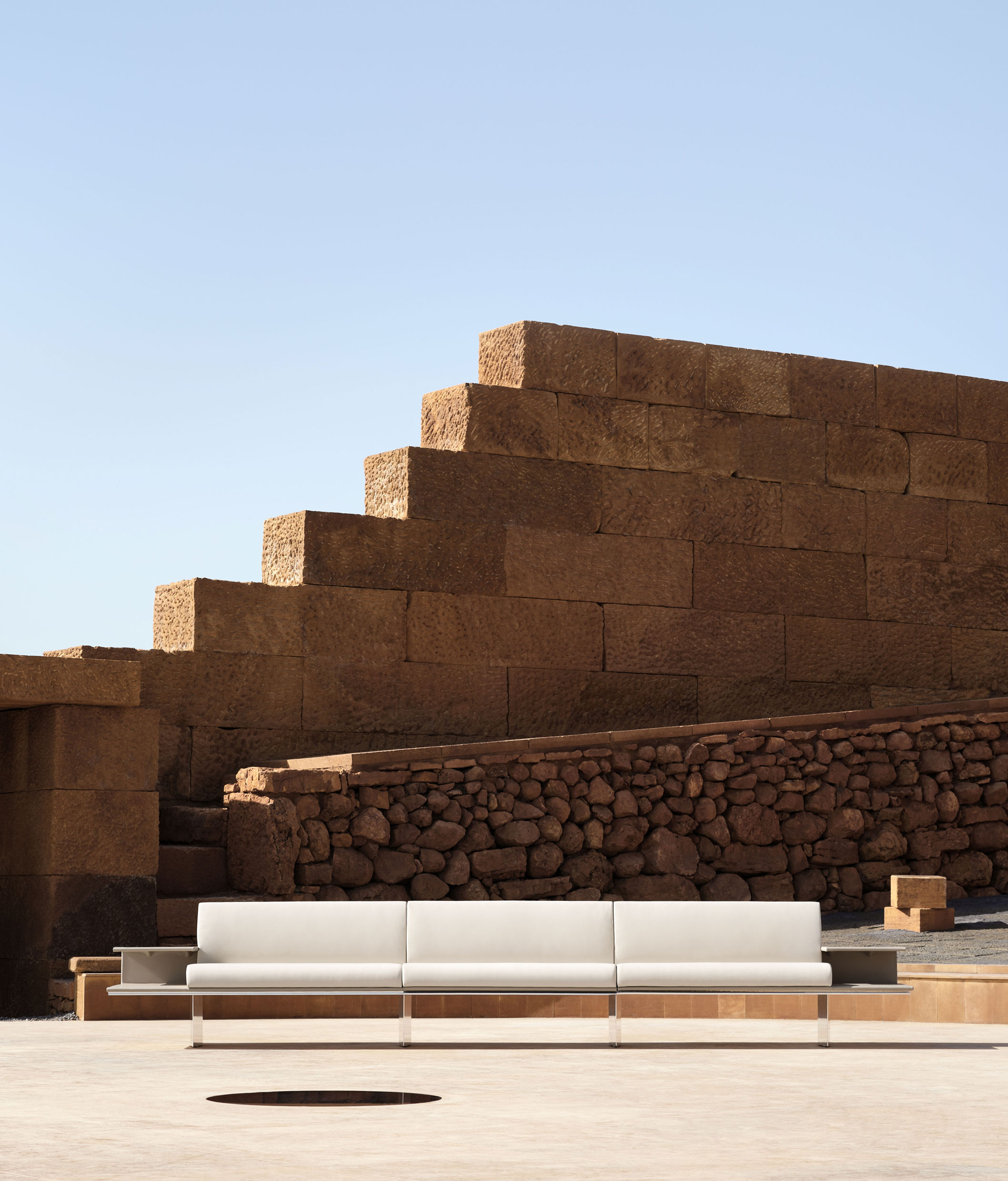 Linear sofa with cantilevered leather covered armrest tables at either end – ph. Alberto Strada